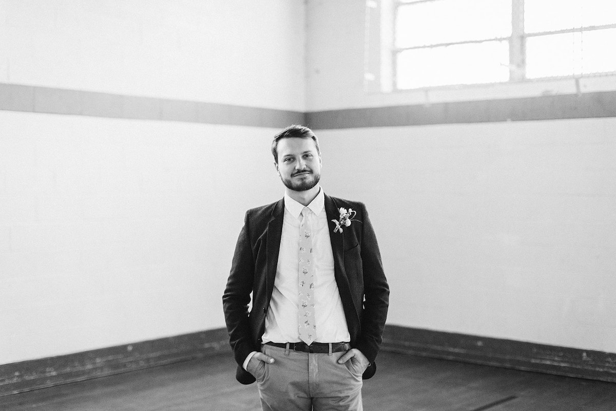 Groom poses in the corner of a gymnasium with his hands in his pockets.