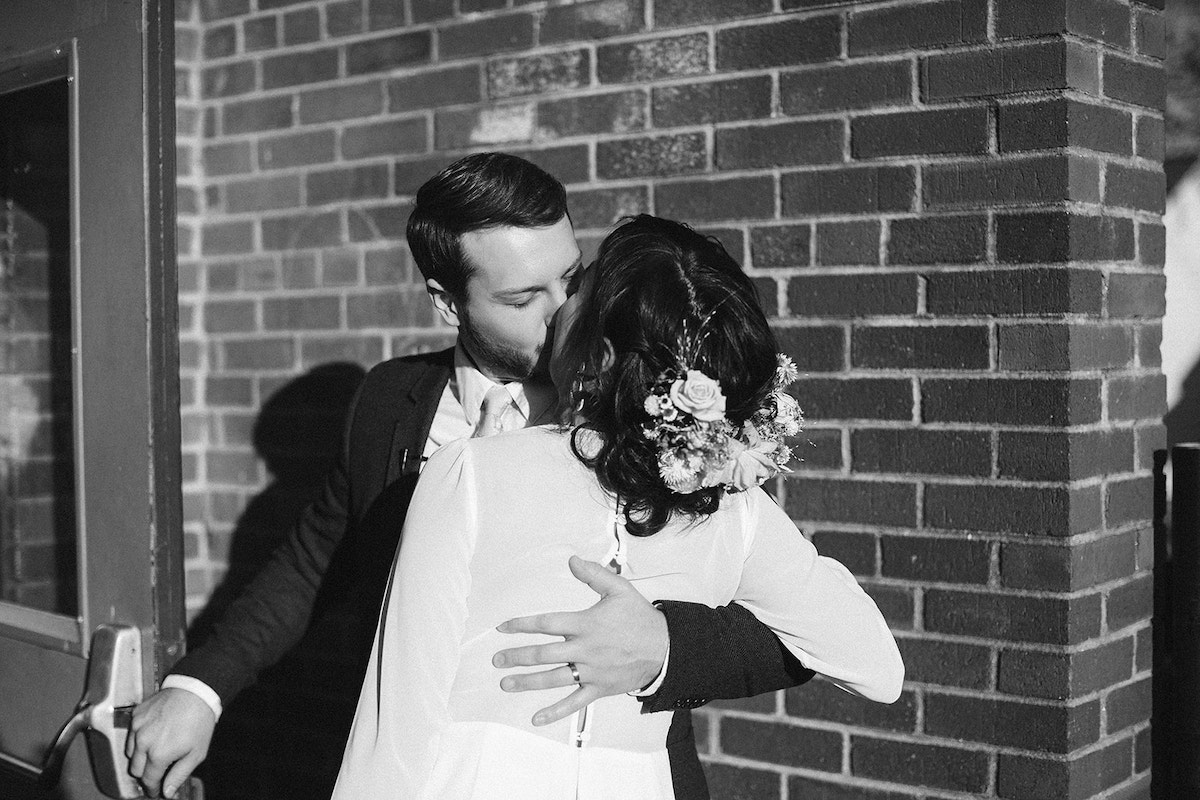 bride and groom kiss in front of a brick wall