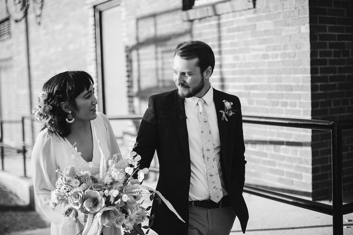 Bride and groom walk along brick building with the shadow of a basketball goal behind them