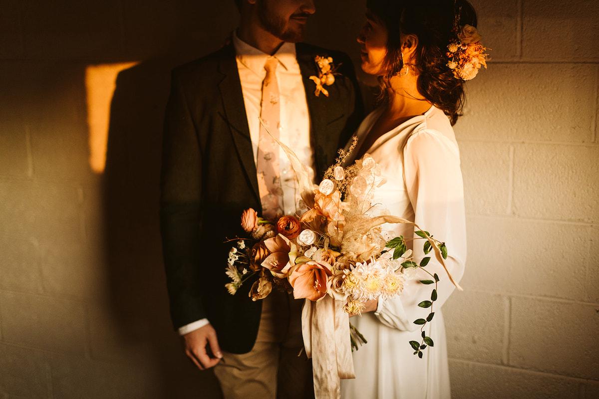 Bride and groom stand against white cement block wall