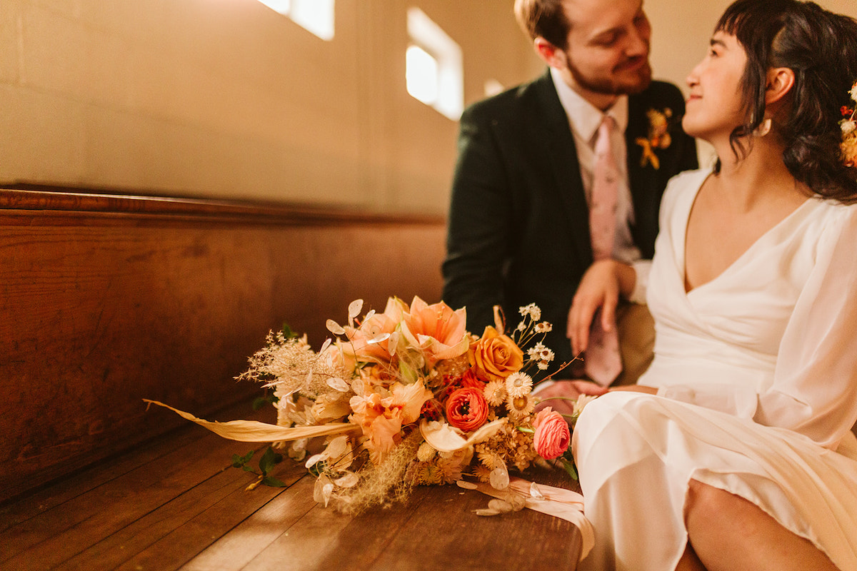 bride and groom sit on wooden gymnasium bleachers with her Southerly Flower Farm bouquet next to them