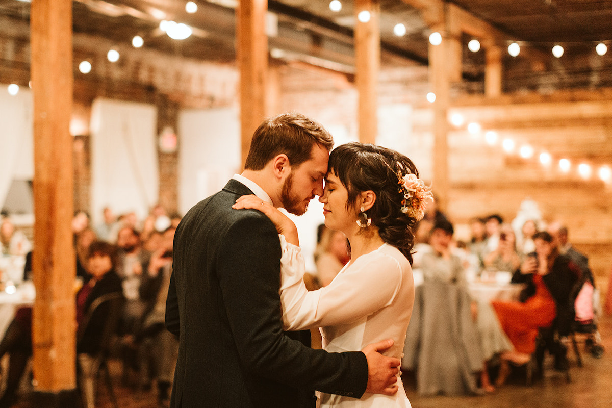 Bride and groom dance with their foreheads touching, her hand on his shoulder and his hand at her waist.