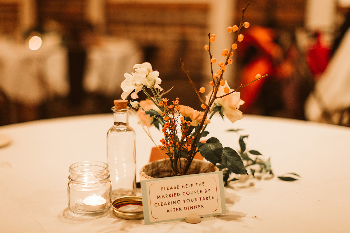 Simple Southerly Flower Farm reception table centerpiece sits between small empty glass bottles and sign for guests
