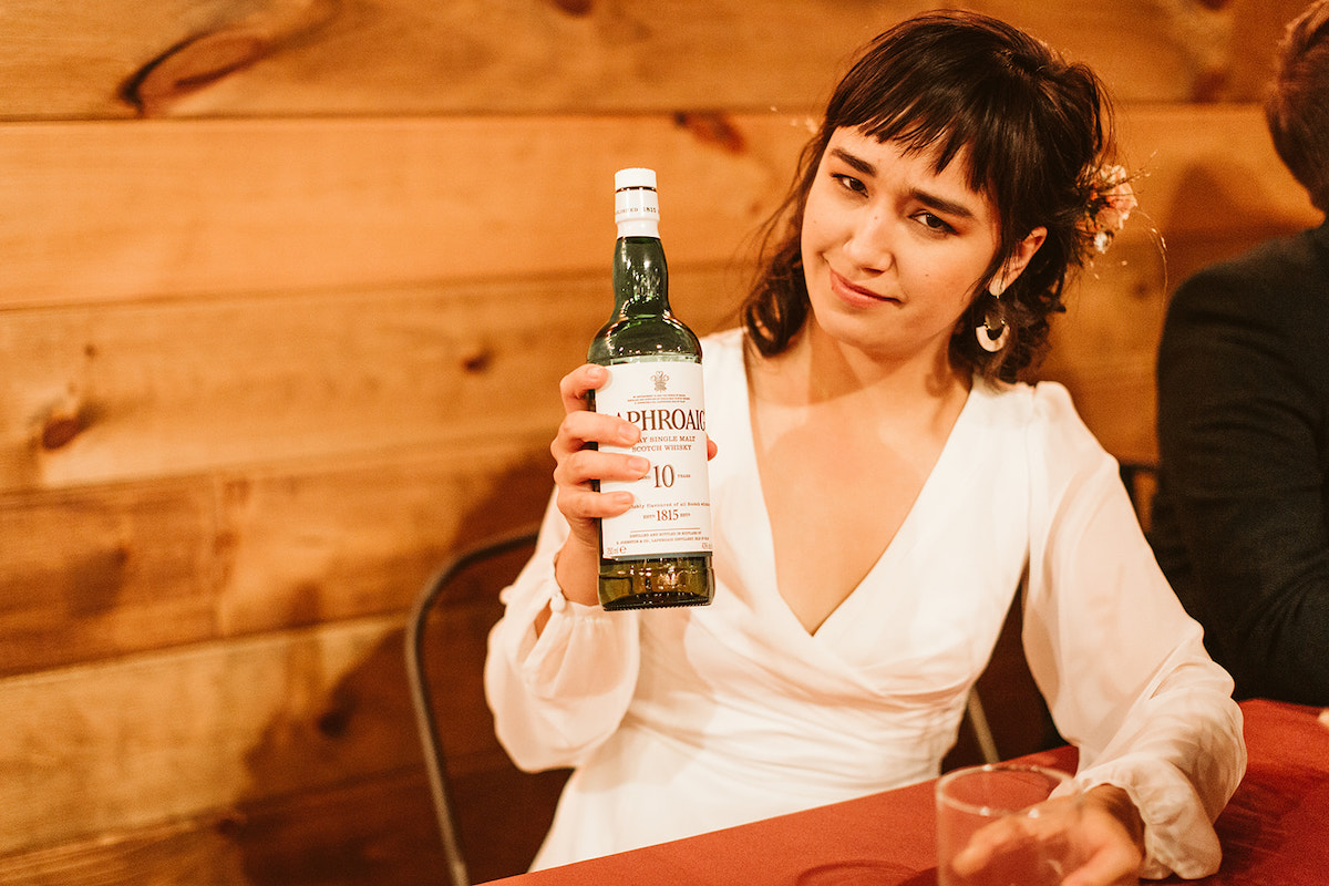 Bride holds up bottle of Laphroaig scotch before toasts