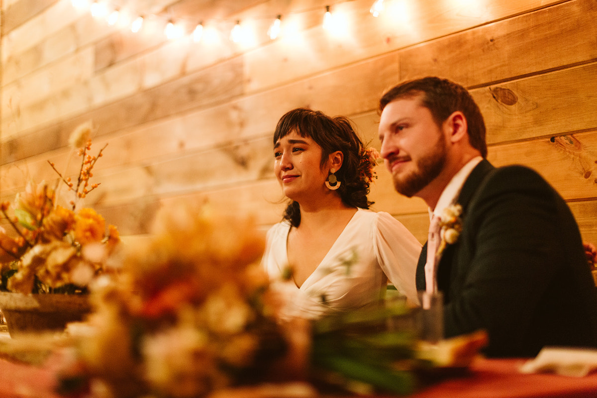 Bride and groom sit in front of shiplap wall. She tears up with emotion.