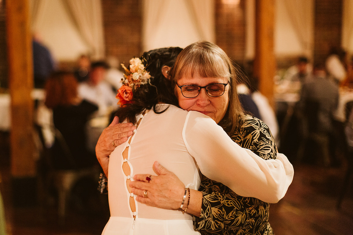 Bride wearing long-sleeve wedding dress with buttons up the back hugs a woman