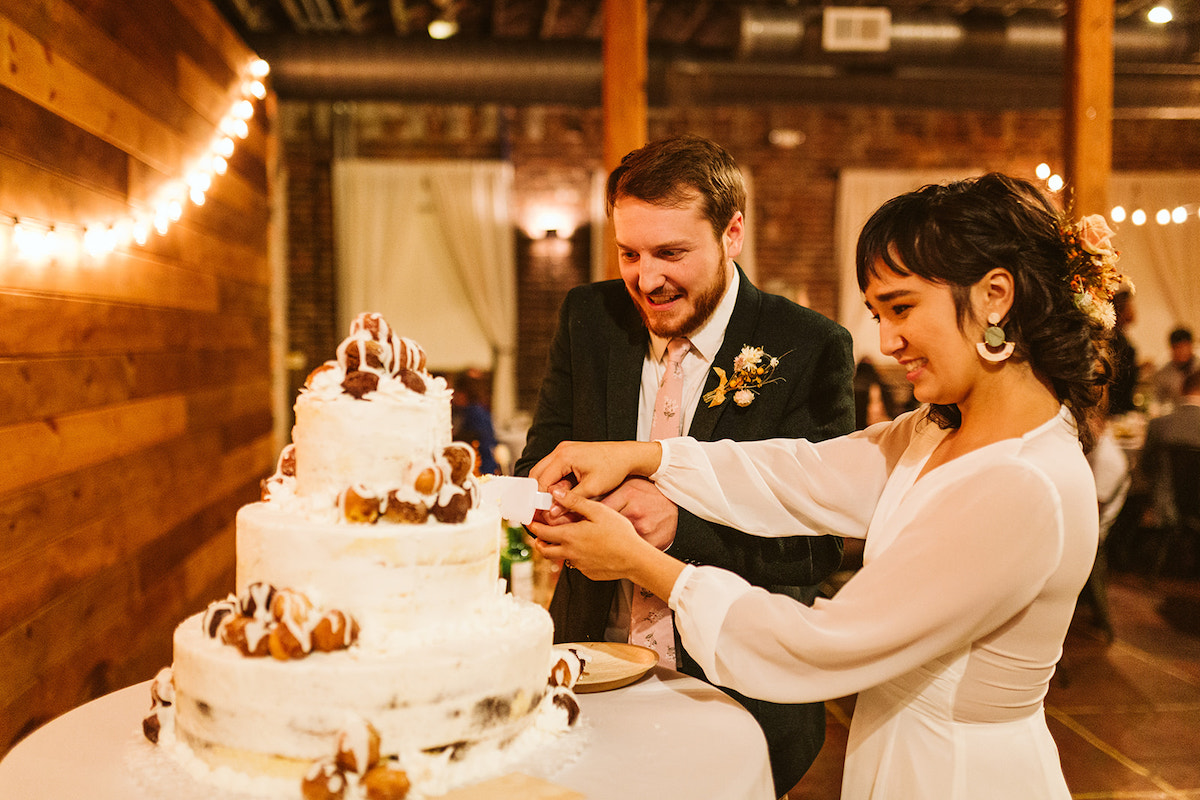 Bride and groom cut into 3-tier cake topped with cream puffs