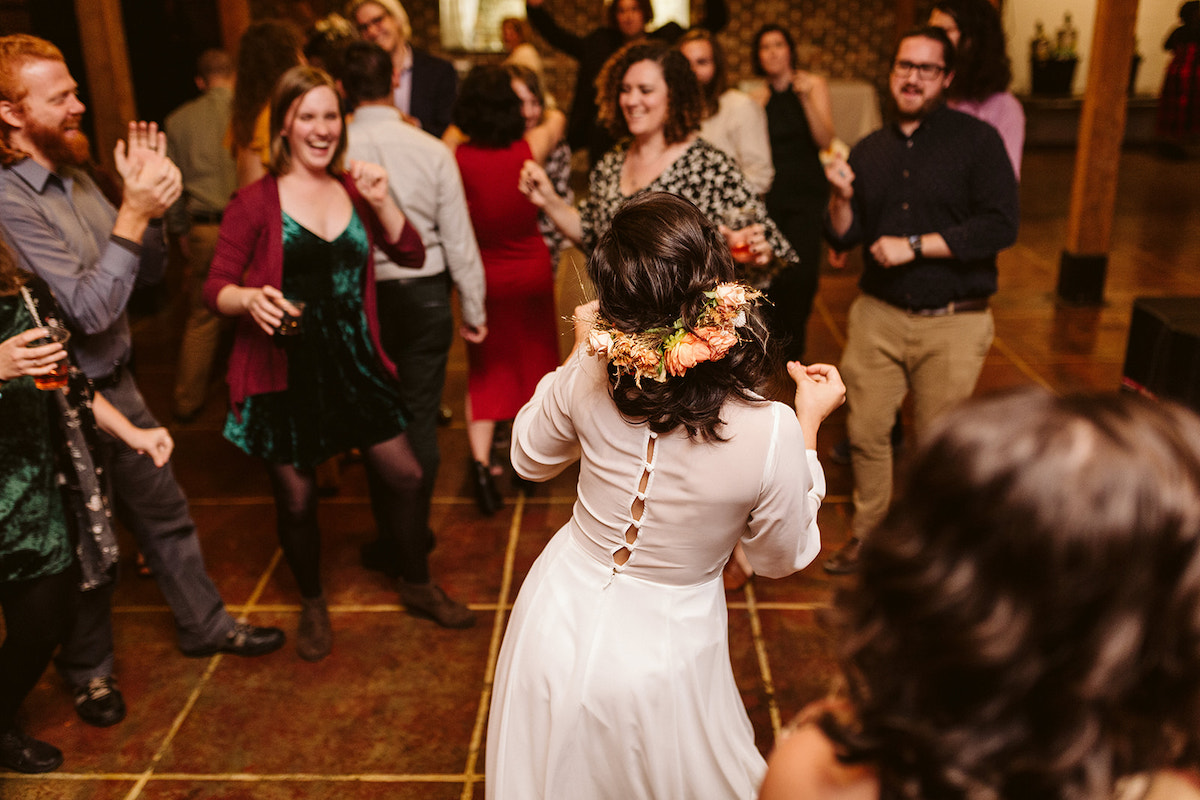 Bride sways in her long-sleeve dress with buttons up the back. She has lots of flowers in the back of her hair.