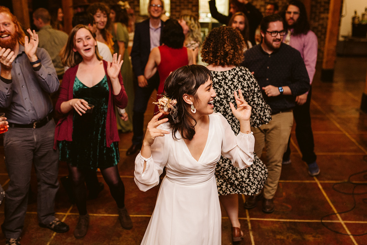 Bride sways in her long-sleeve dress as guests begin to dance around her