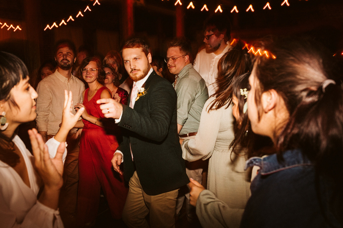 Groom points at bride as they dance together with friends around them at The Old Woolen Mill
