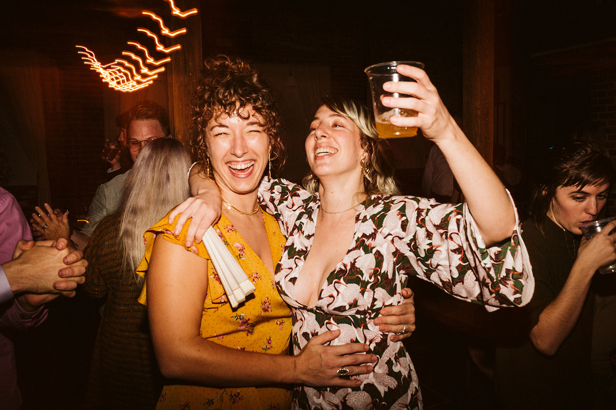 Two women hug and laugh, one raises her cup in a toast