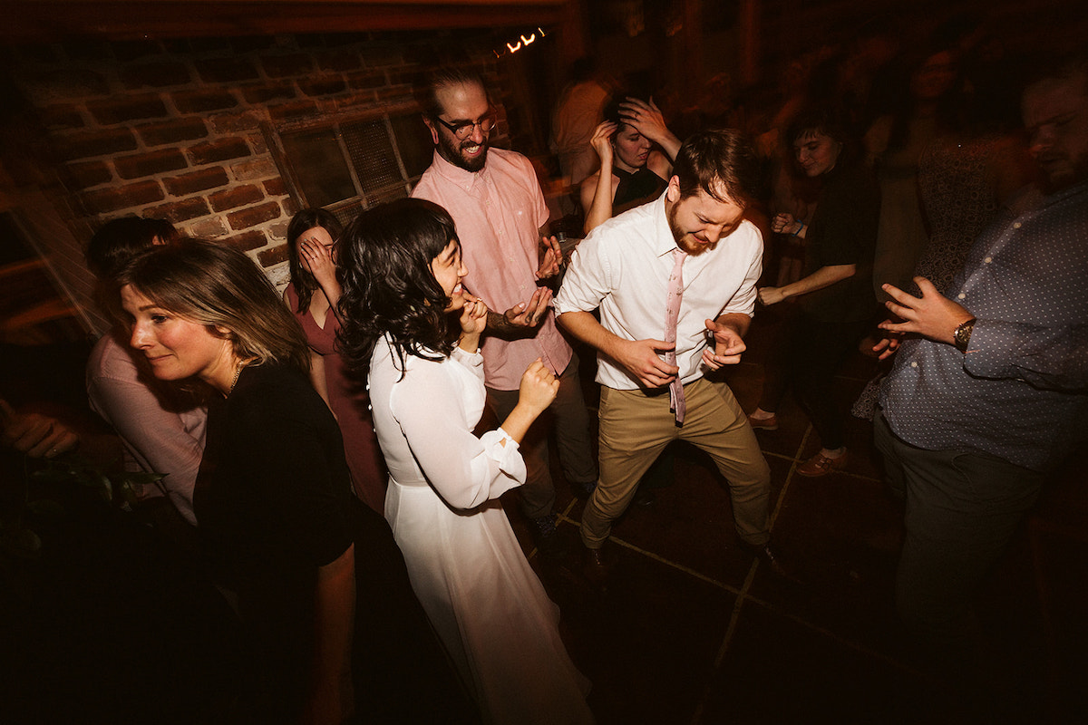 Bride and groom dance, and he plays an air saxophone while friends play other air instruments