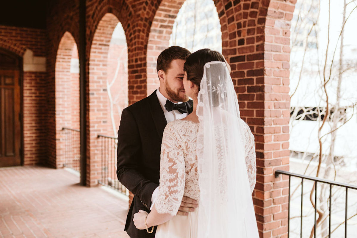 Bride and groom nuzzle under covered walkway between brick archways