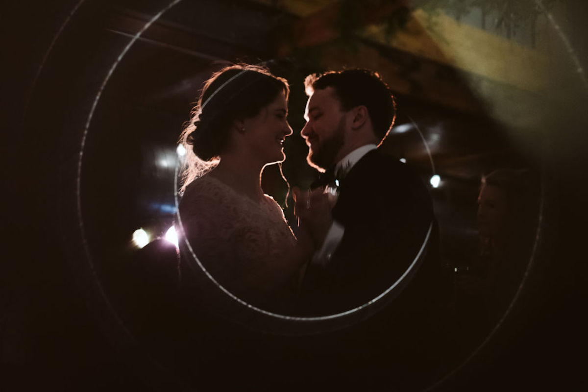 Bride and groom dance in a dark room under the glow of a few spotlights