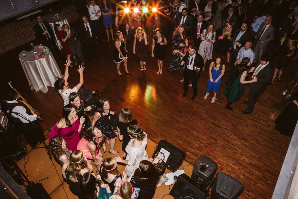 Bride and several female friends sing and dance on band's stage while groom and guests watch and dance on the dance floor
