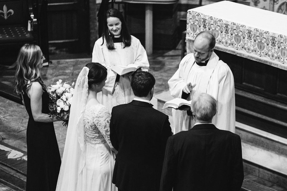Bride and groom stand before priest as he reads from the Bible during their wedding ceremony