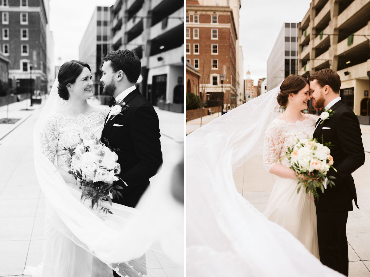 Bride and groom smile at each other between downtown buildings as her veil swirls around them.