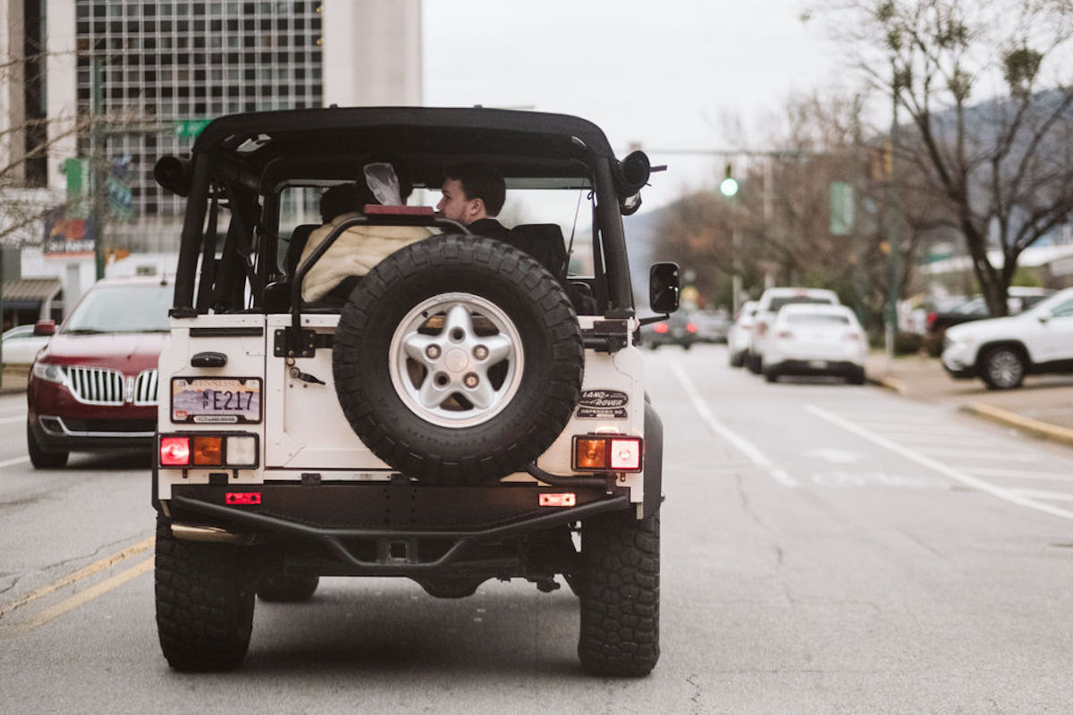 Bride and groom ride in the back of a white jeep