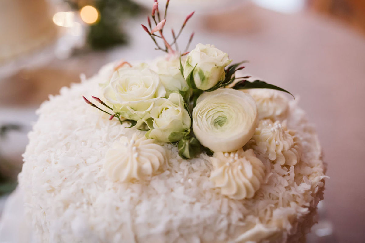 Several small white and pink flowers top a cake covered in coconut flakes