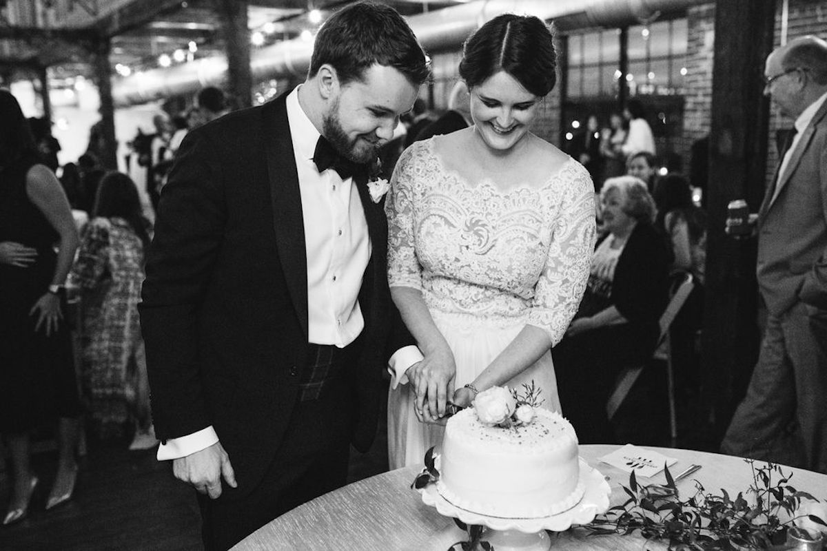 Bride and groom smile and cut into their white frosted cake together