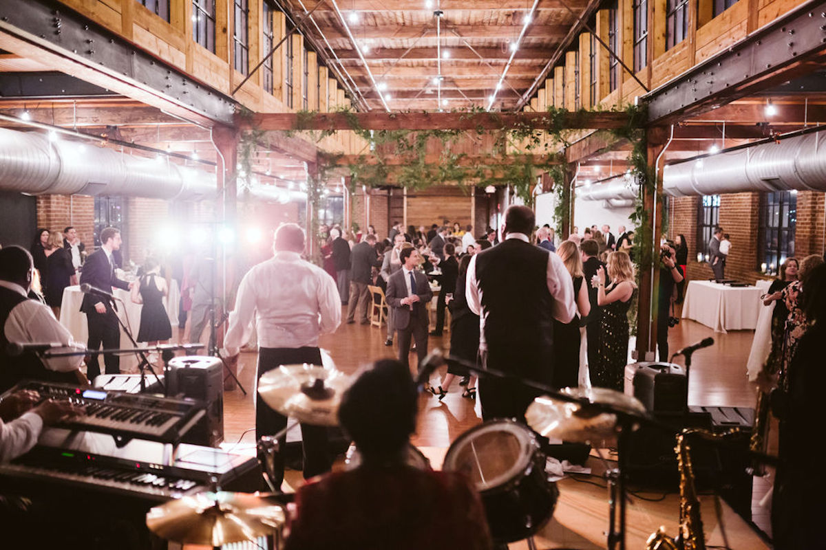 Band plays on stage for wedding guests under exposed beams and ductwork at wedding at The Turnbull Building in Chattanooga TN