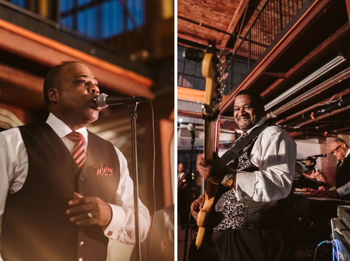 Man wearing black vest and striped tie sings into microphone; another man wearing paisley vest plays bass guitar