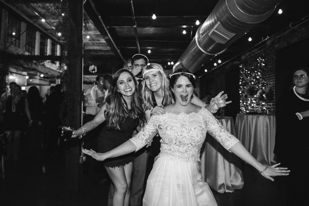 Bride and friends wearing glow sticks like halos under industrial exposed ductwork in warehouse wedding reception