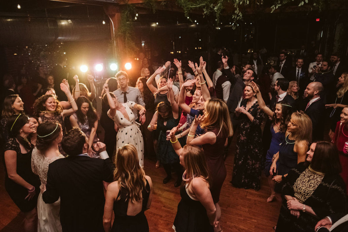 Wedding guests dance in a circle with the bride and groom; greenery hangs from exposed beams at The Turnbull Building