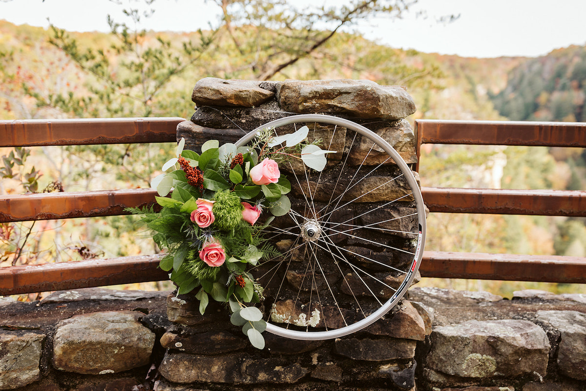 metal bicycle wheel lined with greens and flowers hangs on a stone pillar at Fall Creek Falls intimate wedding ceremony
