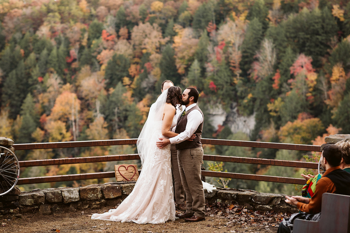 bride and groom kiss in front of a wooden fence during their autumn wedding at Fall Creek Falls State Park in Tennessee