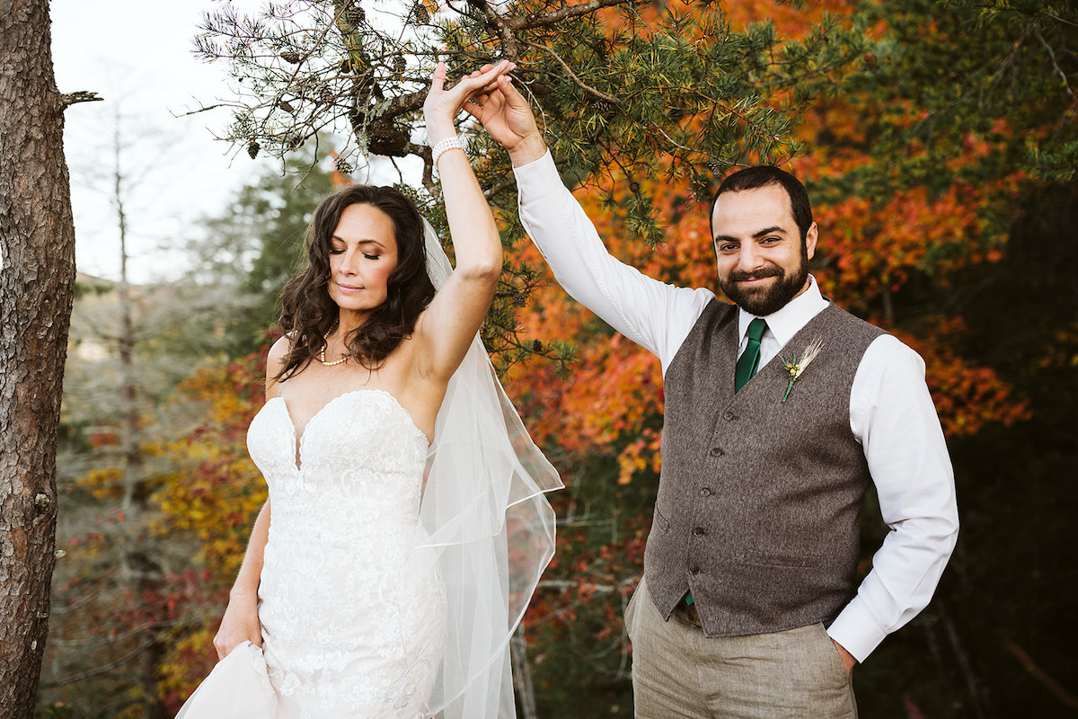 groom wears a brown vest and green tie and twirls his bride in front of brightly colored autumn leaves at Fall Creek Falls