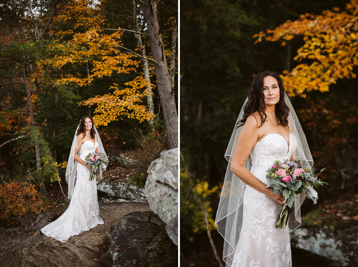 bride in strapless dress holds bright bouquet and stands on large rock in front of colorful autumn leaves