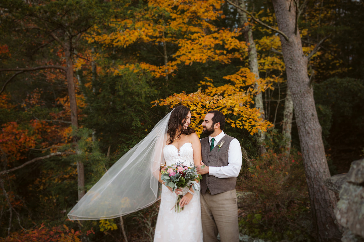 Bride and groom stand together in front of tall tress with colorful autumn leaves at Fall Creek Falls