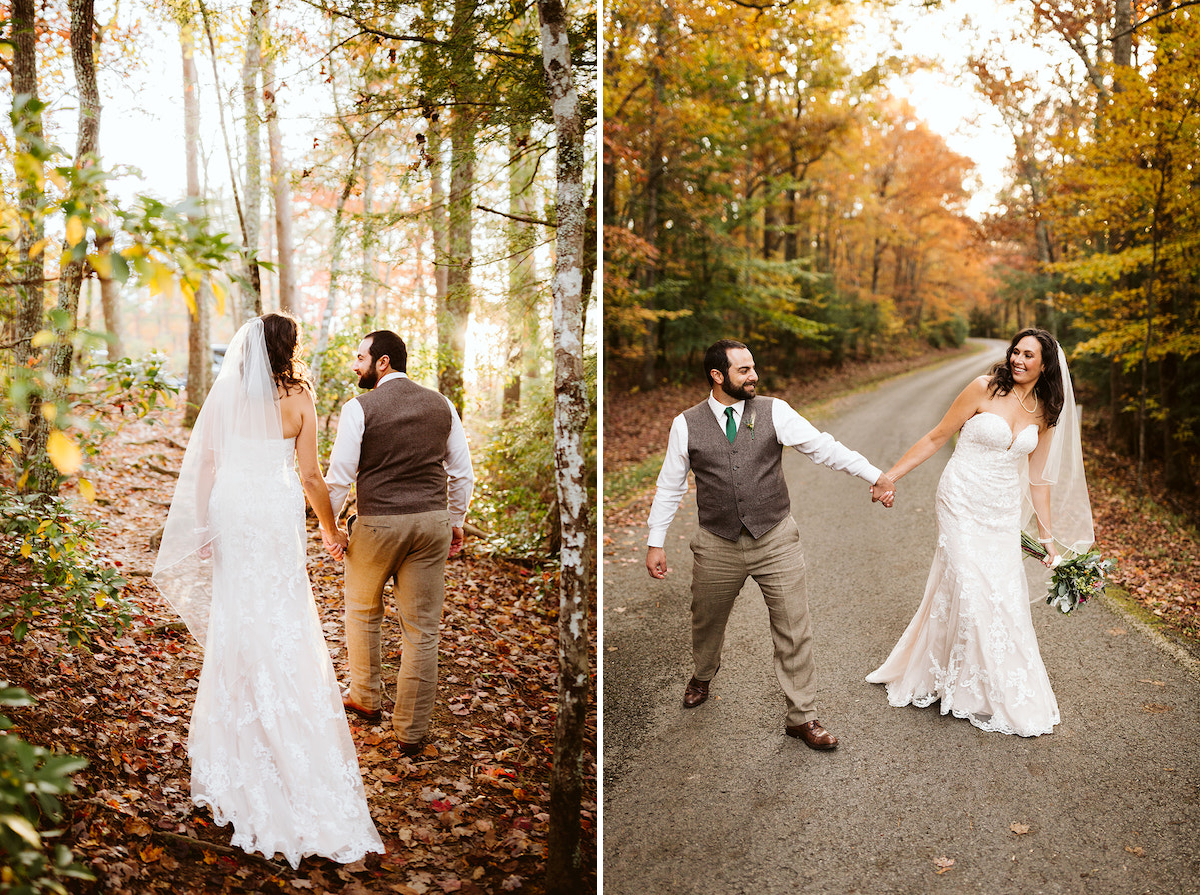 bride and groom hold hands and walk along leaf-covered trail. under tall trees with colorful foliage