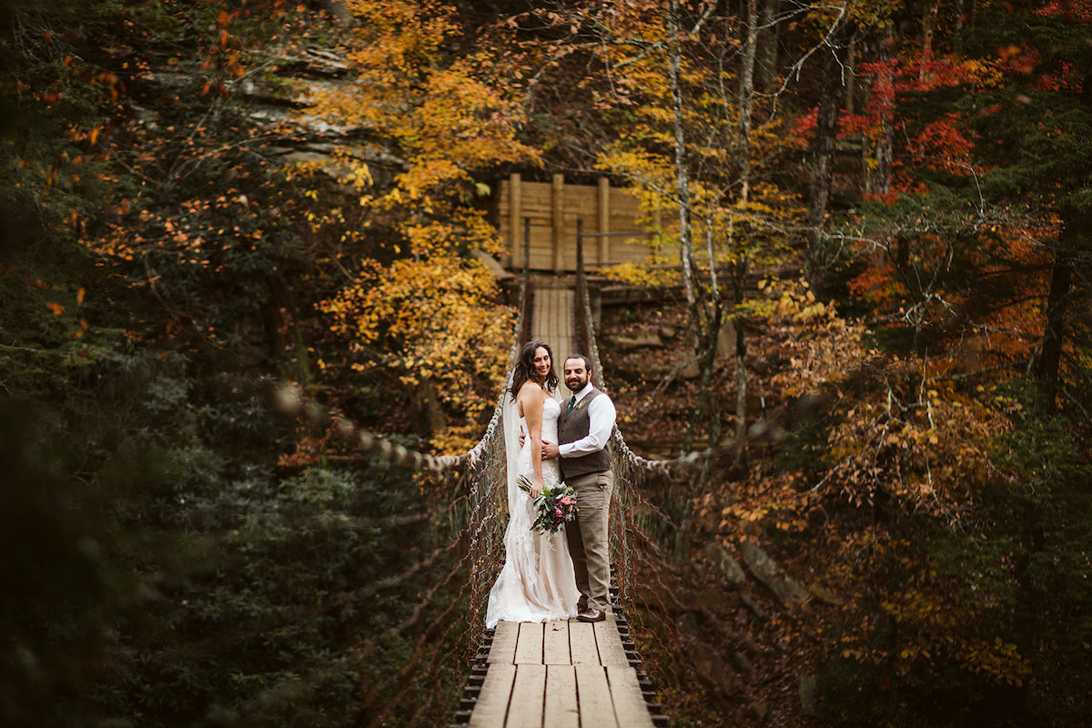 bride and groom stand on a wood and wire suspension bridge at Fall Creek Falls State Park in Tennessee.