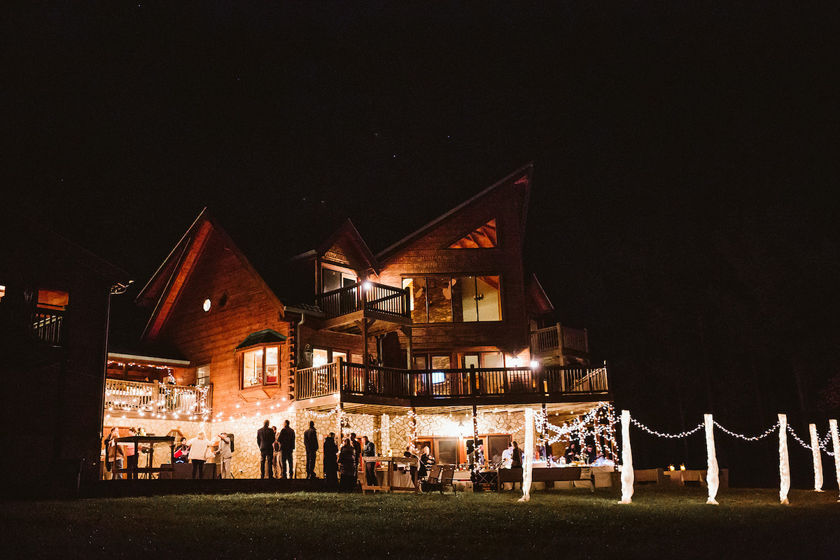 Large angular cabin lit up with patio lights and interior lights against the dark sky