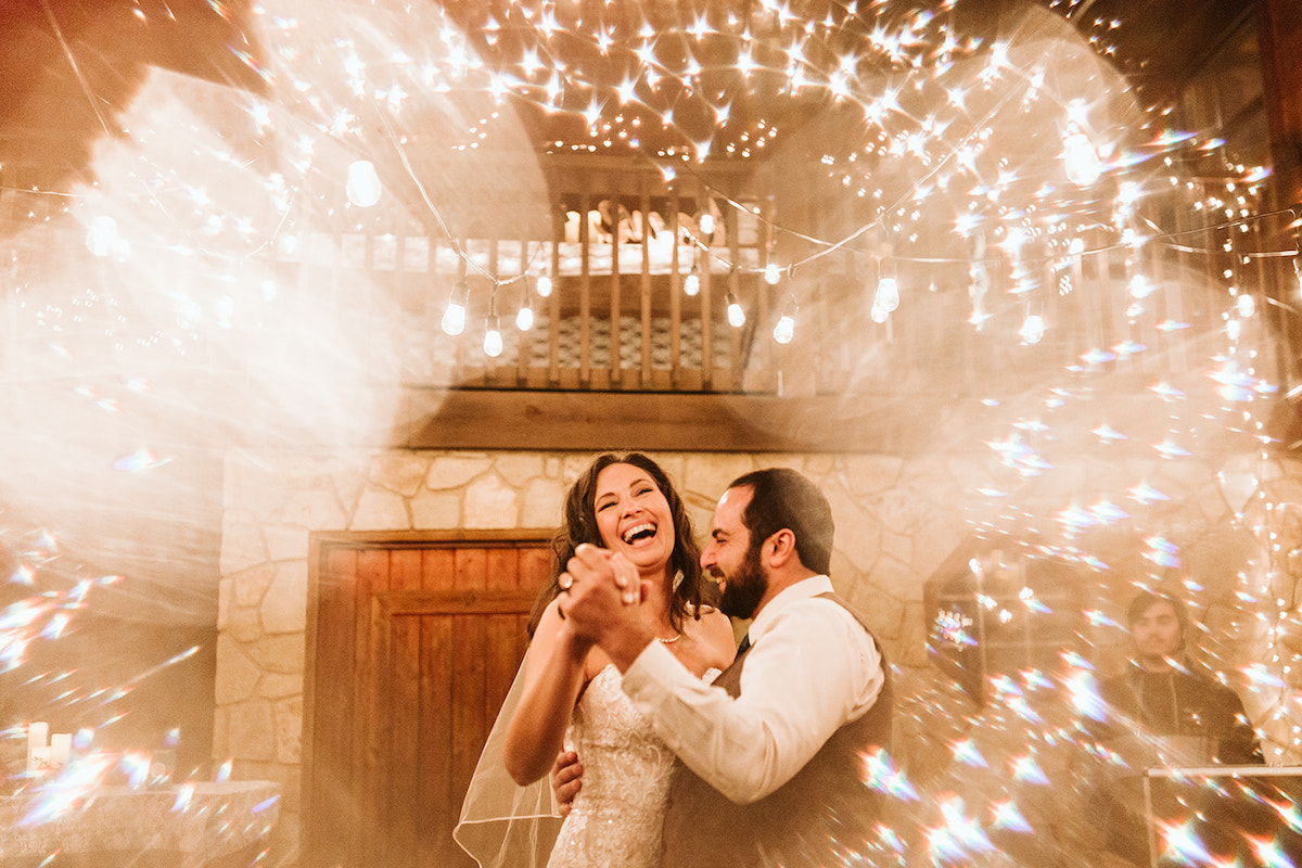 Bride and groom laugh during first dance under white string patio lights