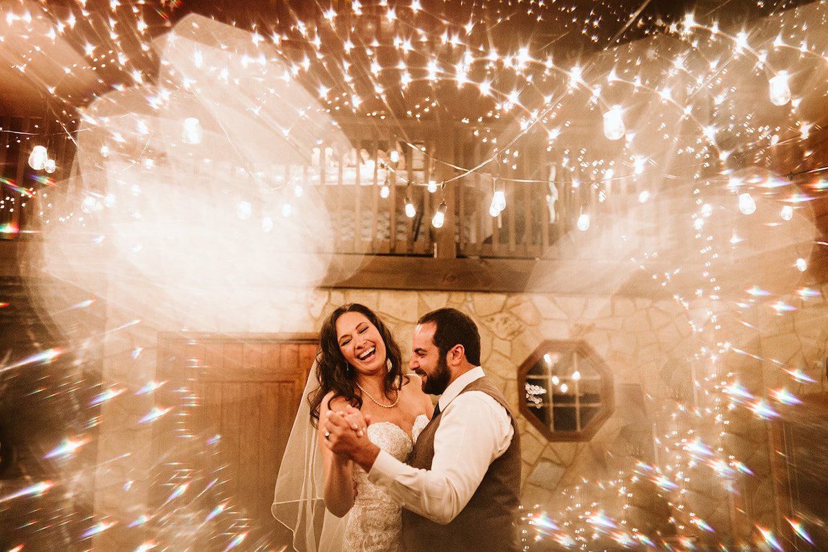 Bride and groom laugh during first dance under white string patio lights