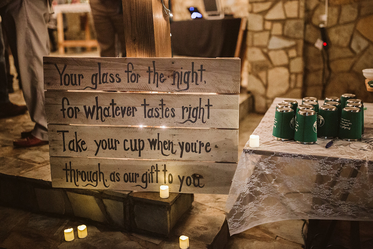 painted wooden sign telling guests to take a metal cup with koozie for the evening and as a wedding favor