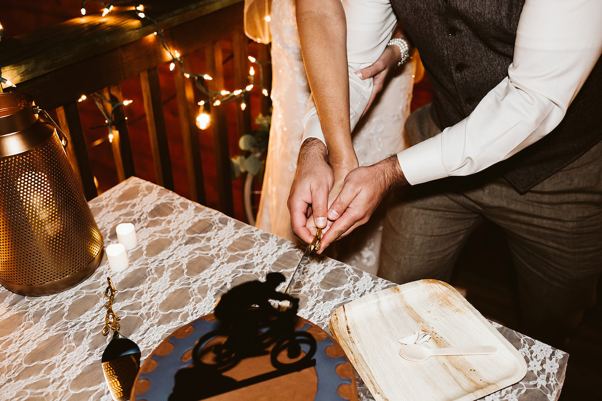 bride and groom cut into chocolate cake topped with bike rider as cake topper