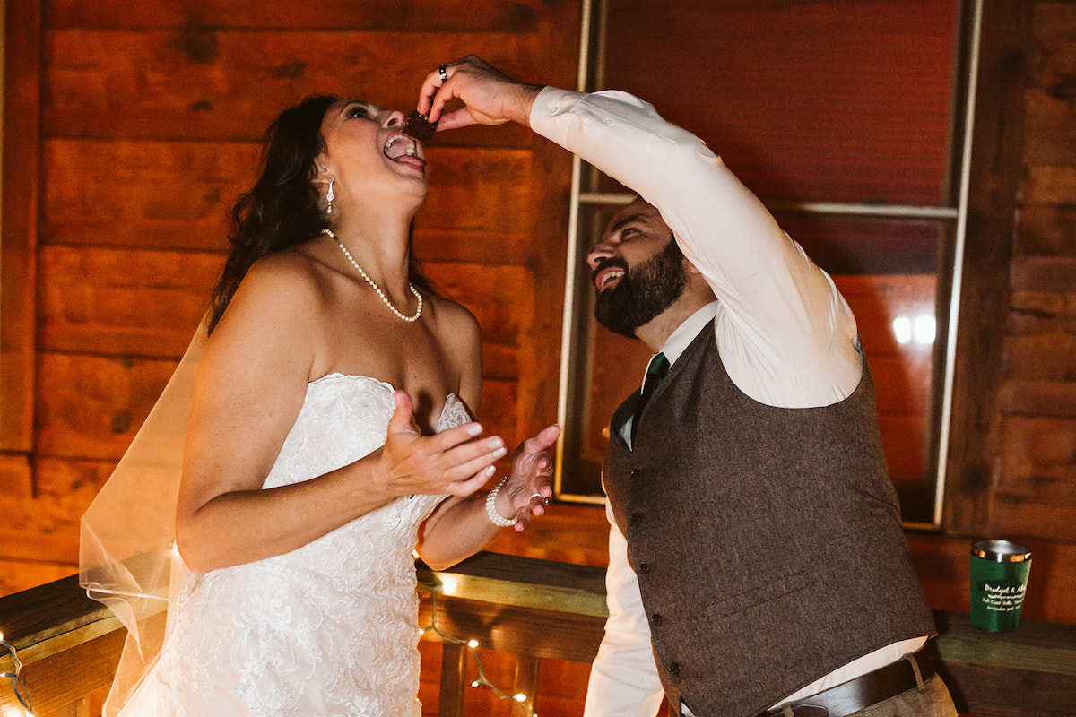 bride lifts her chin as groom in tweed vest reaches to feed her cake