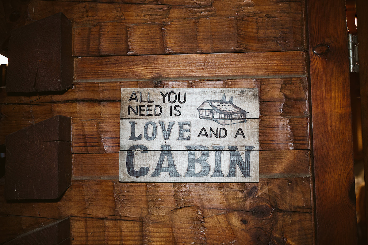 wooden sign painted with "All you need is love and a cabin" hanging on a rough wooden wall