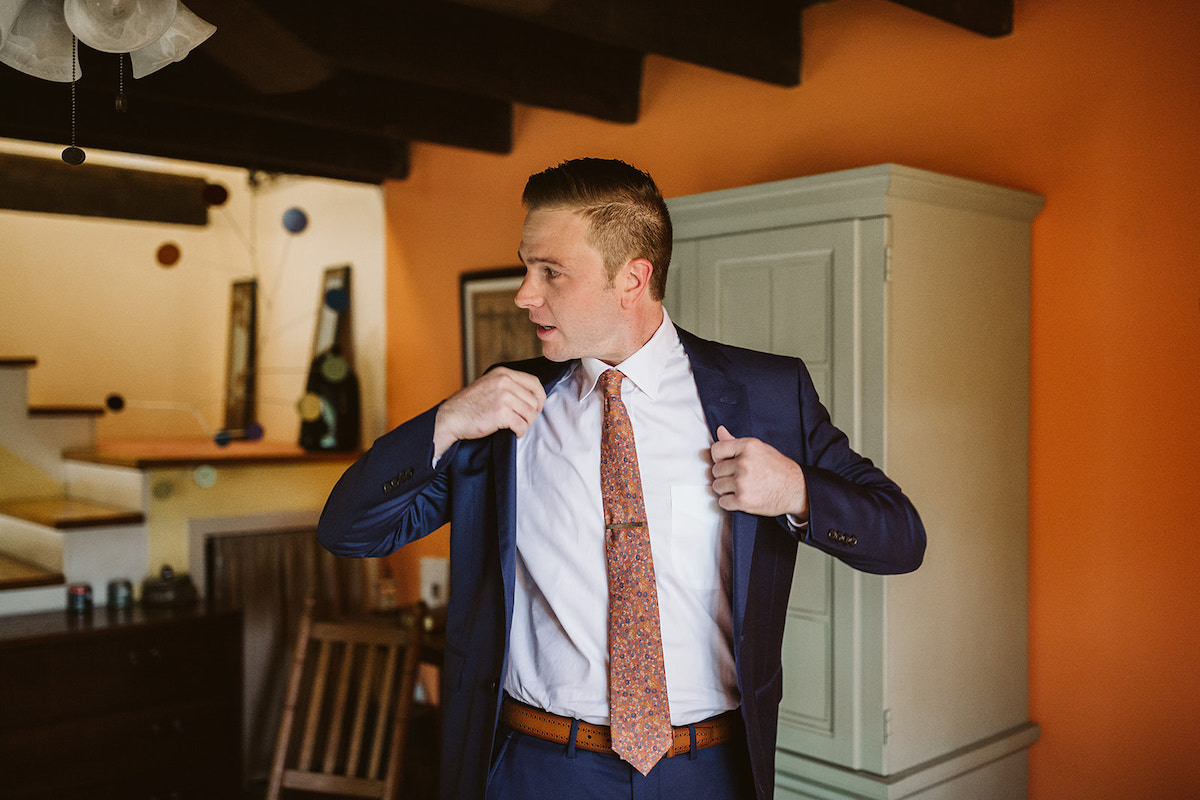 Groom straightens his deep blue suit coat over his white shirt