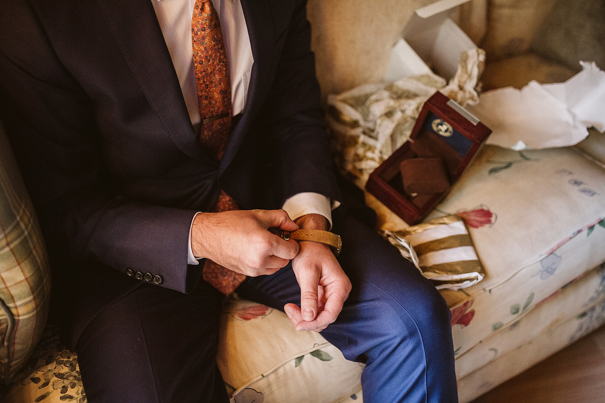 groom sits on floral sofa and fastens his watchband