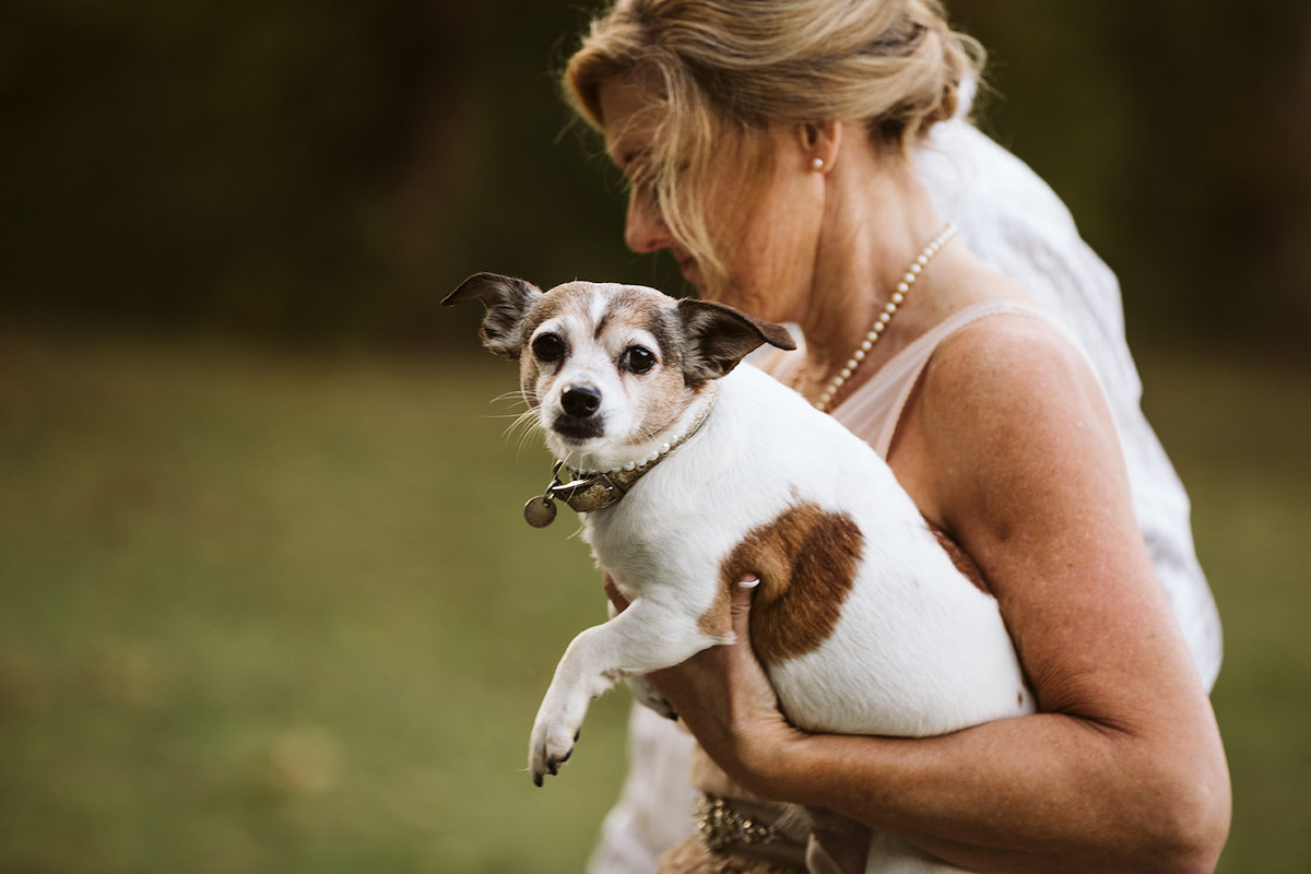 woman in sleeveless shirt carries a small white and brown dog