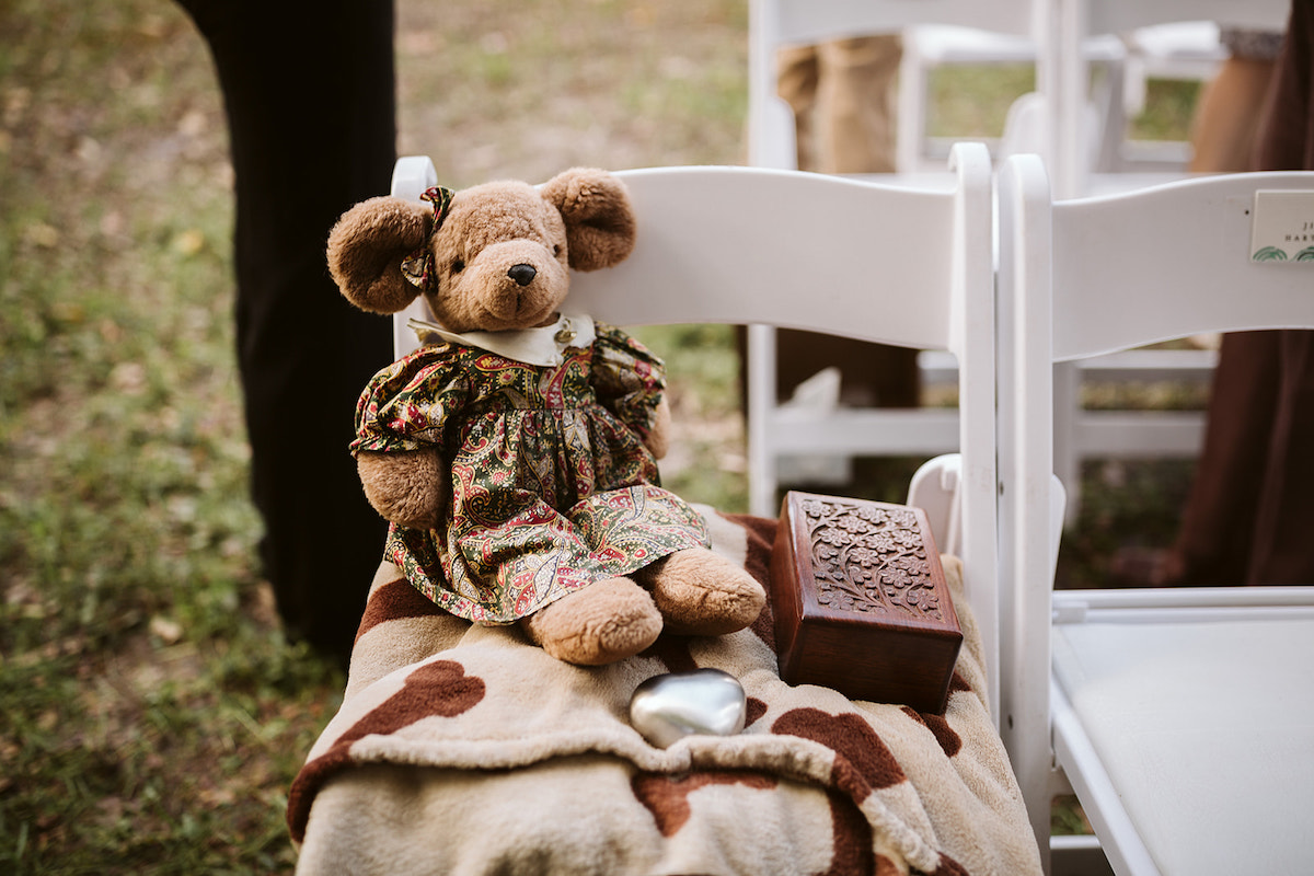 stuffed bear and wooden box sit on top of a blanket in a folding white chair