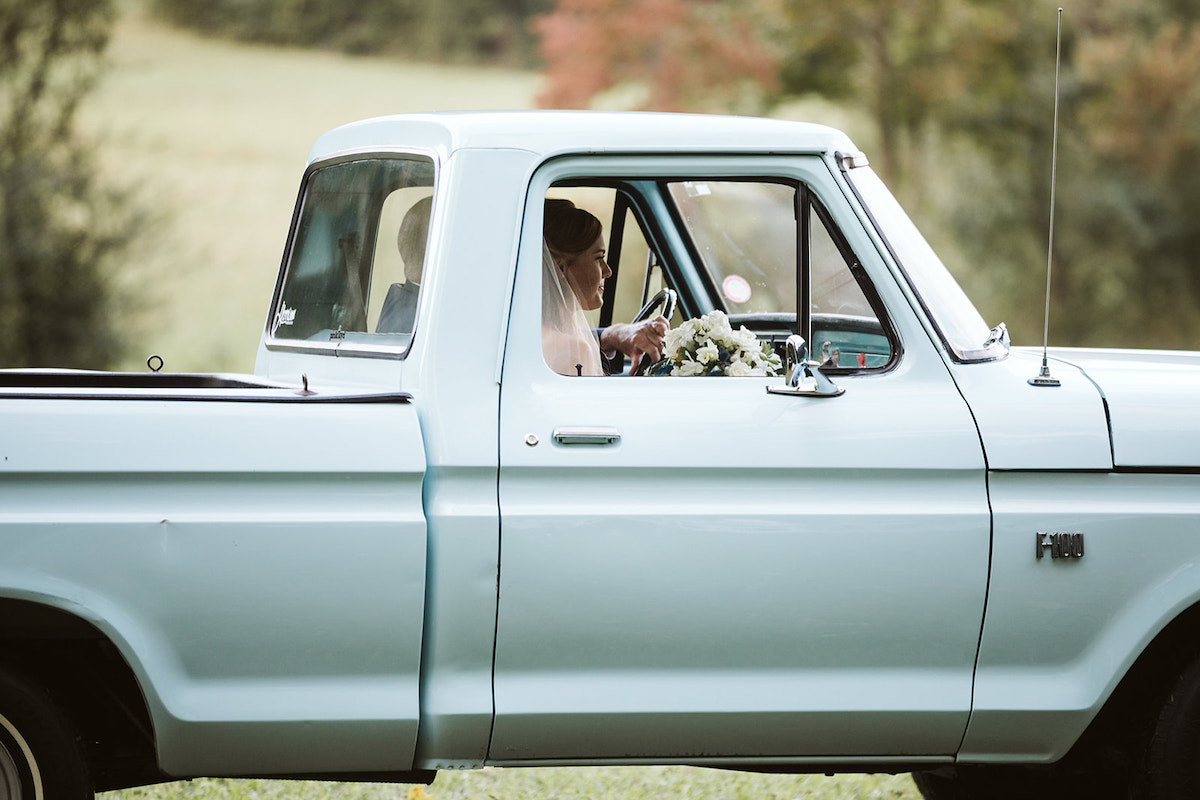 bride holds bouquet of white flowers and sits in passenger seat of an antique baby blue Ford F-100 pickup truck