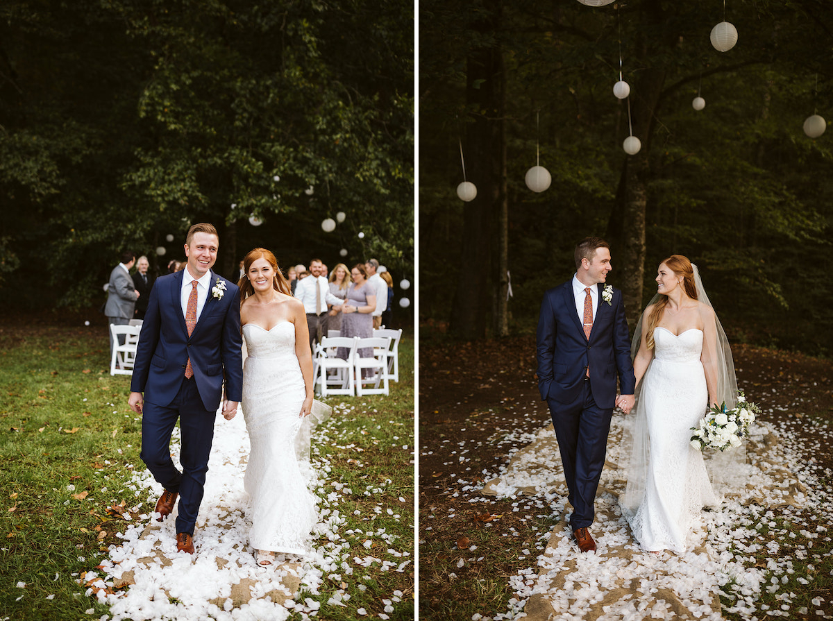 bride and groom walk between white folding chairs, holding hands. A large tree strung with white paper lanterns is behind them.