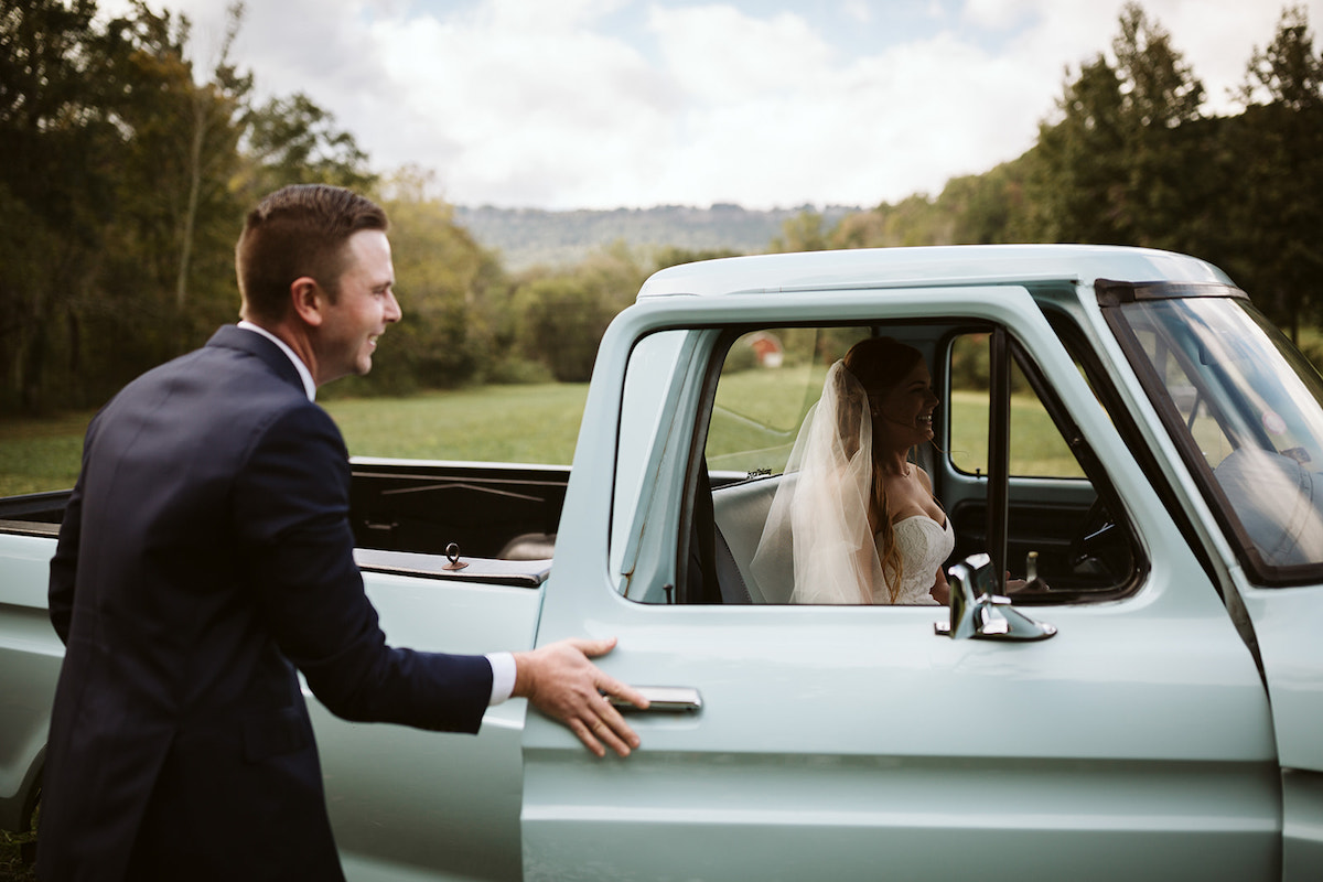 groom shuts the door of his antique baby blue Ford pickup truck while bride sits inside, smiling