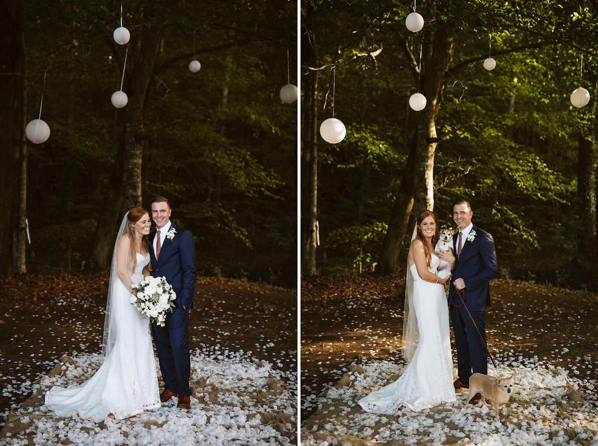 bride and groom stand on a bed of white petals beneath tall green trees hung with white paper lanterns